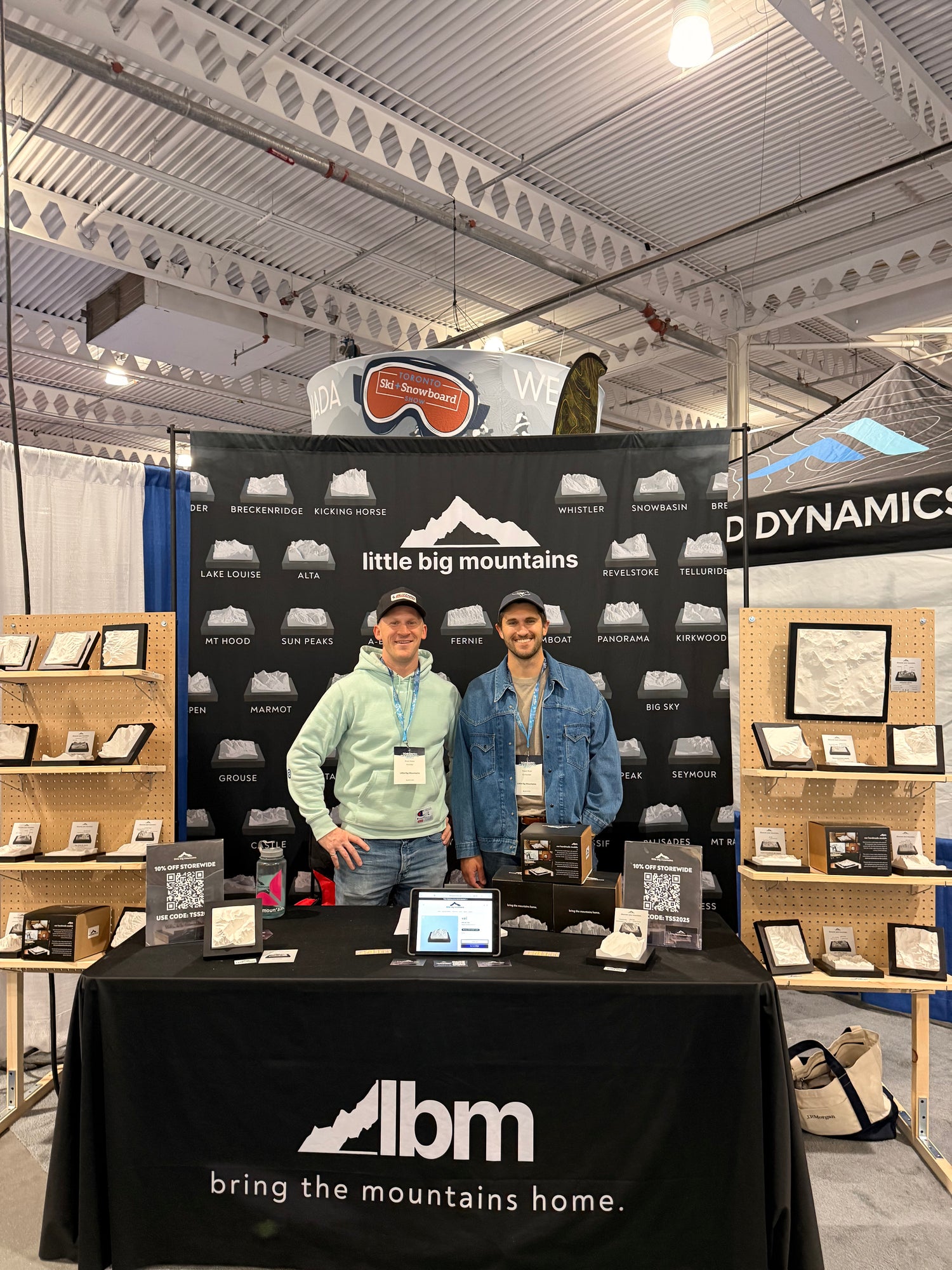 Two men standing at a booth surrounding by mountains.