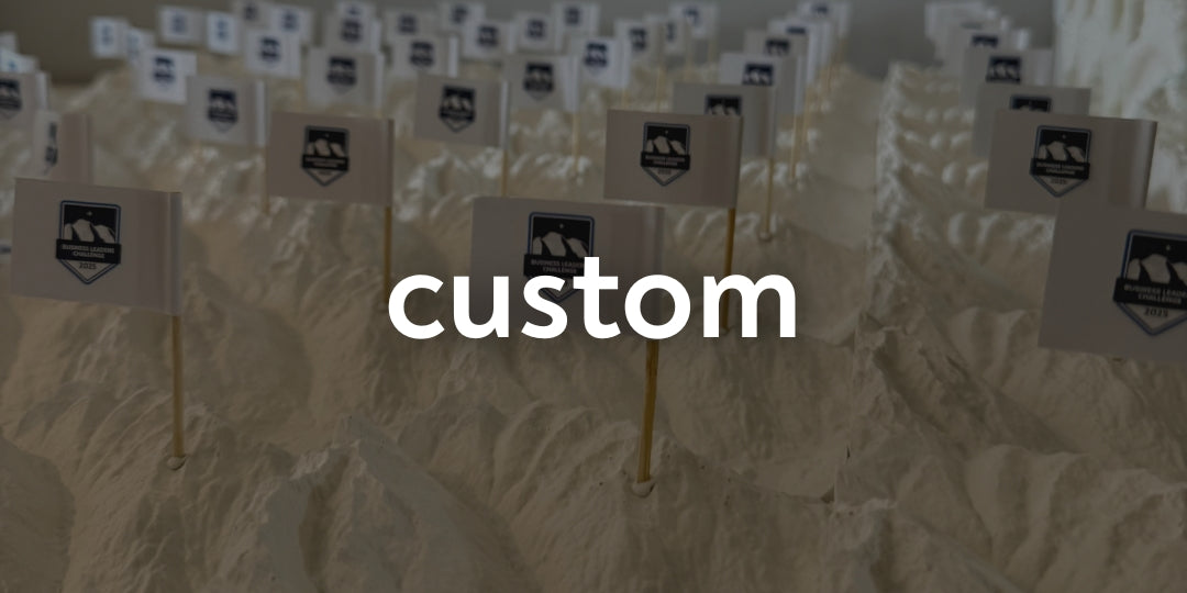 Flags with a logo and the word 'custom' overlaid on a mountainous landscape.